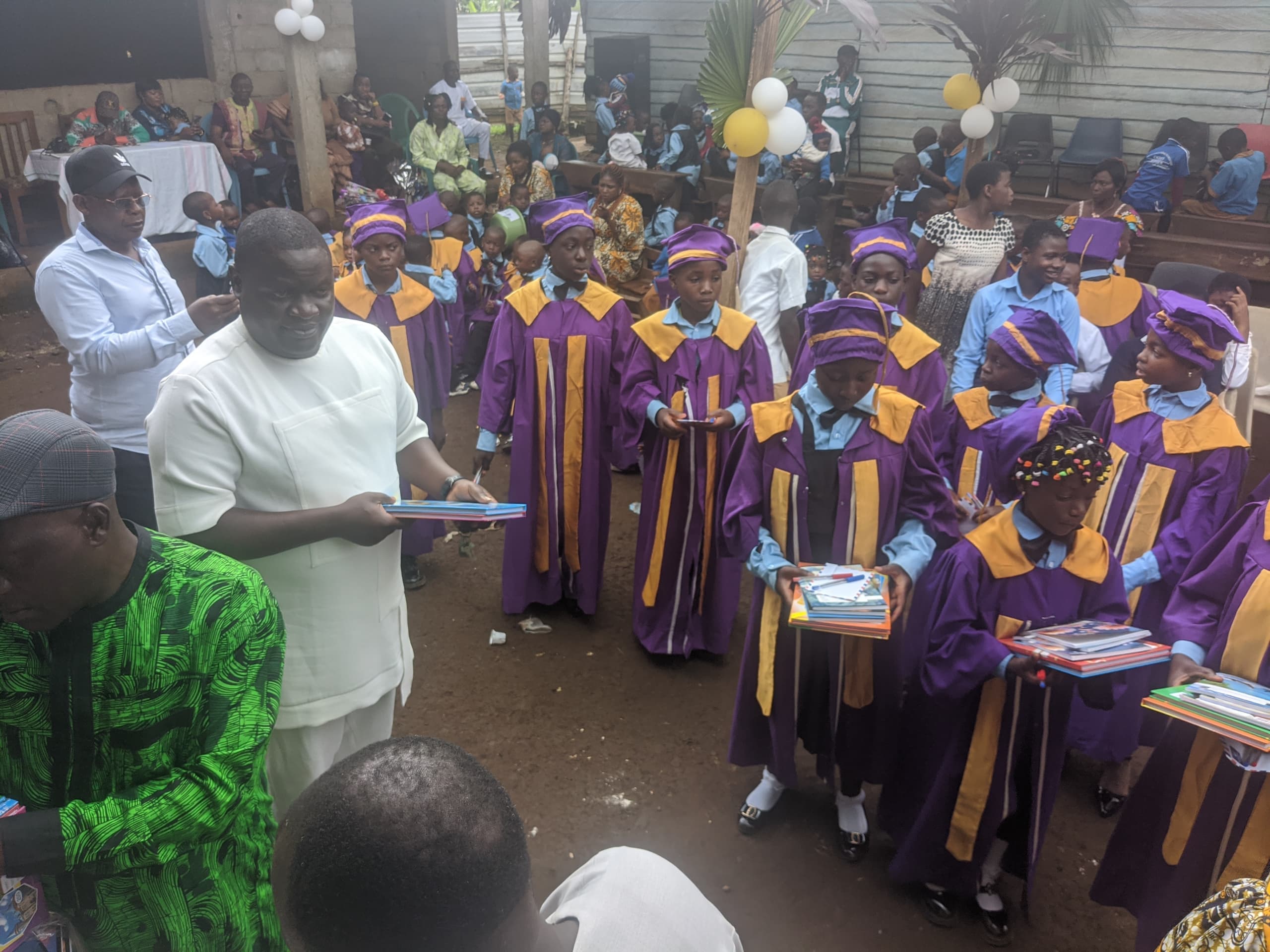 Mr Metuge Armstrong distributing notebooks to pupils in purple graduation gowns